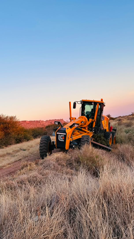 Motor grader clearing bush at sunset