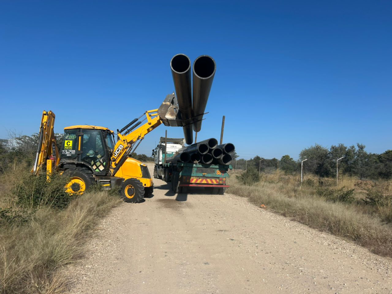 Backhoe loader carrying pipes on a gravel road